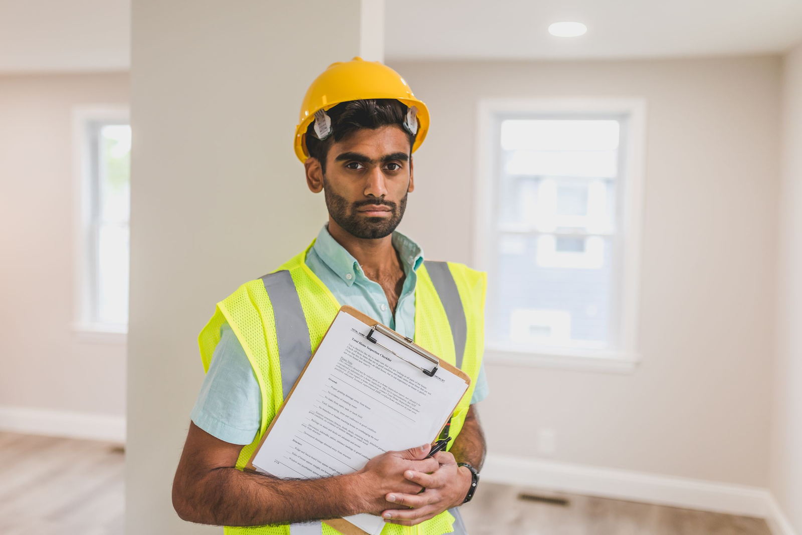 Site engineer in a hard hat and hi-vis vest holding an inspection clipboard on a plant floor
