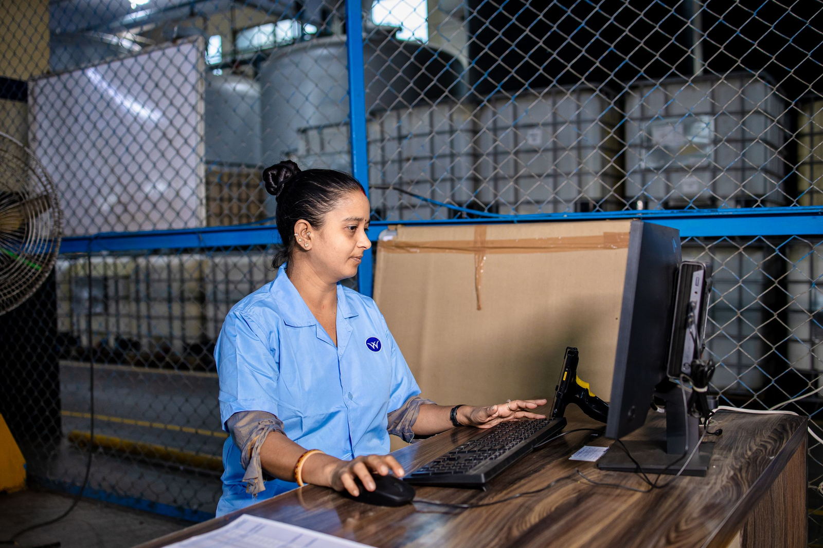 Warehouse coordinator in uniform working at a computer and barcode scanner beside stored stock