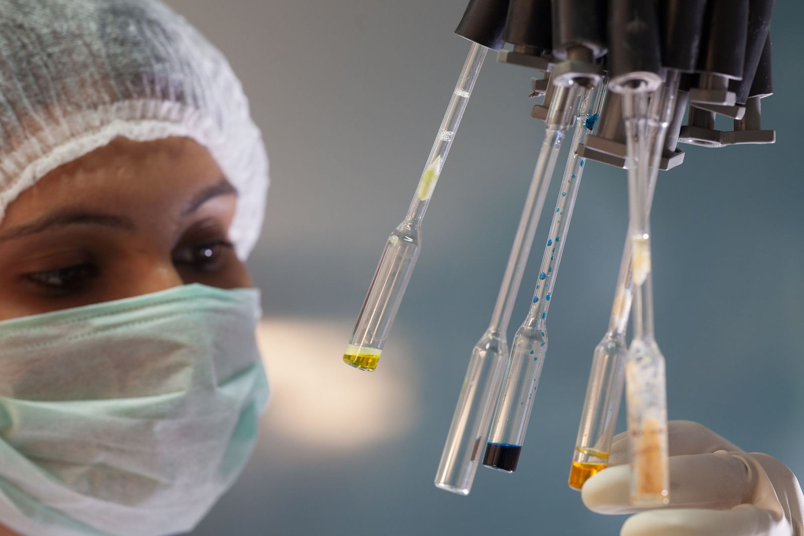 Technician in cap, mask and gloves inspecting glass ampoules in a pharmaceutical lab