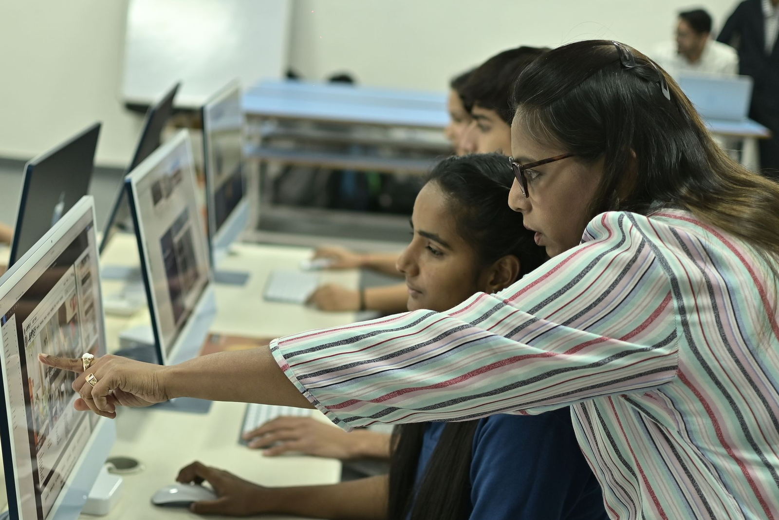Trainer guiding a student at her screen in an institute computer lab